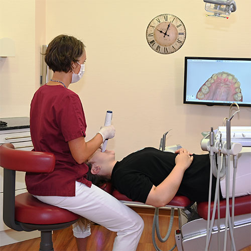 Eine Mitarbeiterin scannt den Kiefer einer Patientin, die auf einem Behandlungsstuhl liegt, der gescannte Kiefer wird auf einem Monitor angezeigt